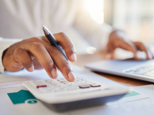 Finance, accounting and fintech, a man on a computer and calculator working out his business budget strategy. Businessman at his office desk, laptop, money management and financial investment online.